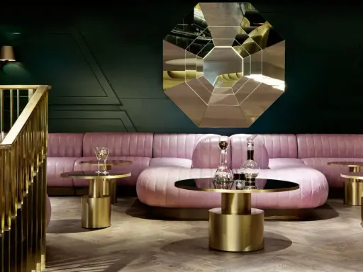 Salon chic avec canapé rose poudré, tables basses dorées et miroir géométrique. Une ambiance **déco belle époque** moderne.