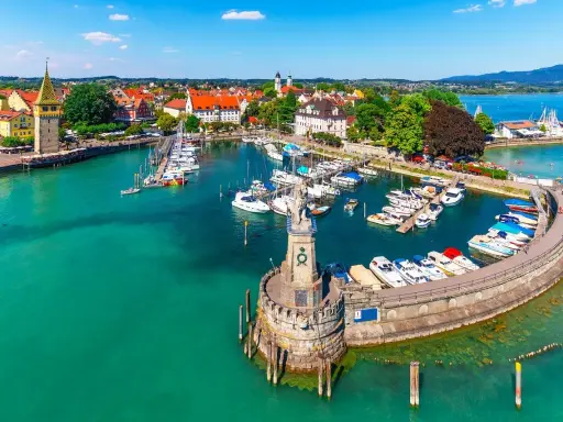 Malowniczy port nad Jeziorem Bodenskim z licznymi jachtami, latarnią morską i zabytkową zabudową miasta.