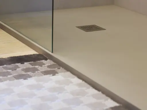 Plato de ducha de resina con desagüe cuadrado. Alfombra a cuadros en primer plano.
