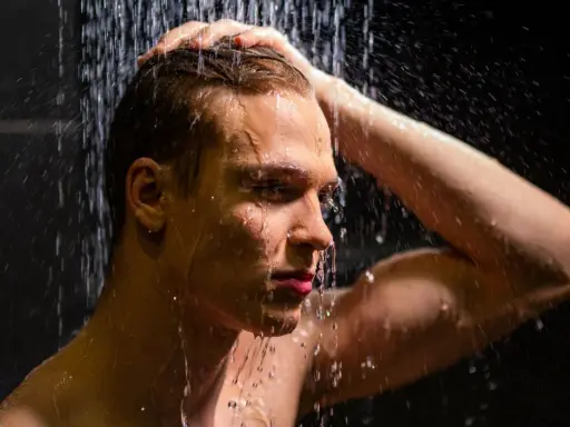 Ein Mann unter der Dusche, der sich die Haare wäscht. Die kalte Dusche ist eine Herausforderung, aber er hält durch.