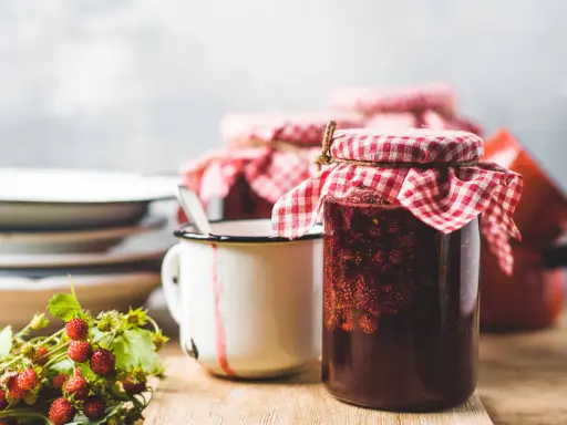 Gläser mit Erdbeermarmelade, bereit zum Marmelade einfrieren. Daneben ein Becher und frische Walderdbeeren.