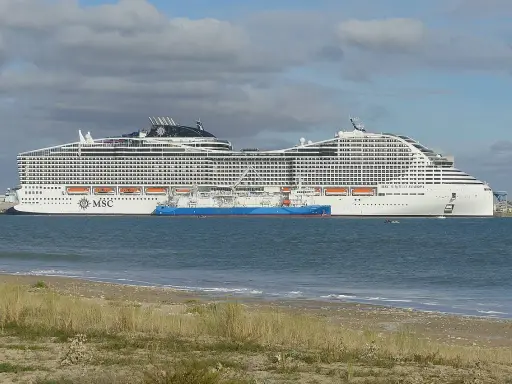 A large white MSC World Europa cruise ship docked next to a blue tanker ship in the sea.