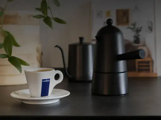 Eine Tasse Lavazza-Kaffee steht neben einer schwarzen Mokkakanne. Die Szene vermittelt die klassische italienische Kaffeezubereitung.
