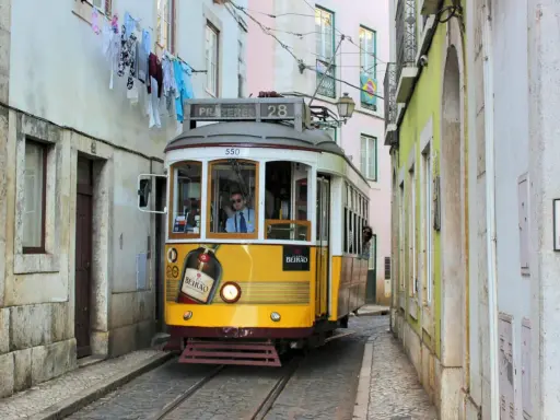 Gelbe straßenbahn lissabon fährt durch enge Gasse, Wäsche hängt über der Straße.