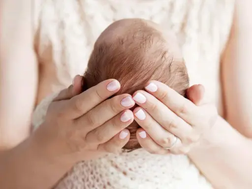 Mani delicate che accarezzano la testa di un neonato, proteggendo la sua fontanella.