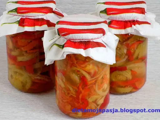 Słoiki z pyszną sałatką z pomidorów na zimę, ozdobione serwetkami z chili.