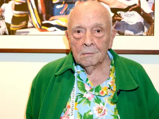 An elderly man with a green jacket over a floral shirt. This image might spark some david bailey interesting facts about his iconic style.