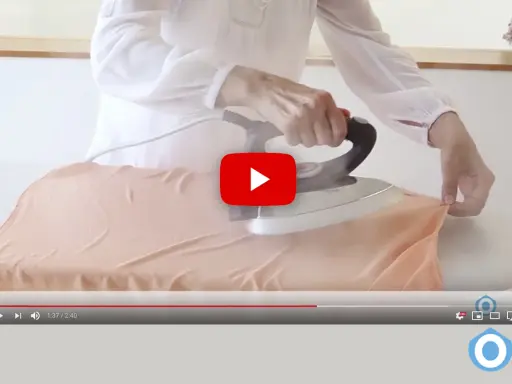 Manos planchando tela de viscosa con vapor en una tabla de planchar.