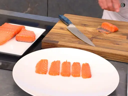 Filetes de salmón marinado listos para servir. Un cuchillo y una tabla de cortar de madera sugieren preparación.