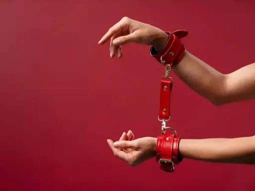 Czerwone kajdanki, symbol bdsm skrót, na nadgarstkach. Dłonie wyciągnięte w geście.