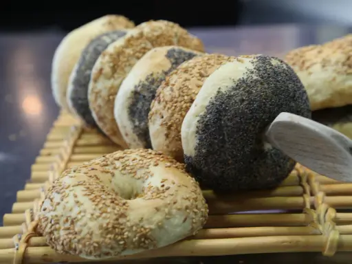 Une rangée de bagels faits maison, certains recouverts de graines de sésame, d'autres de pavot, sur une natte en bambou.