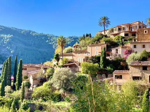 Malerische Häuser mit Zypressen und Palmen, ein grüner Berghang im Hintergrund. Ein friedlicher Anblick von Mallorca im Dezember.