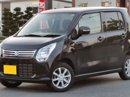 Ciemny Suzuki Wagon R+ z żółtą tablicą rejestracyjną, zaparkowany na ulicy.