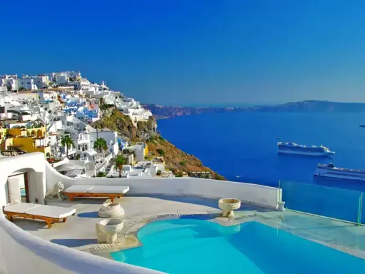 Vista mozzafiato di Santorini con case bianche a picco sul mare blu intenso. Due navi da crociera all'orizzonte, un invito a scoprire crociere a prezzi stracciati.