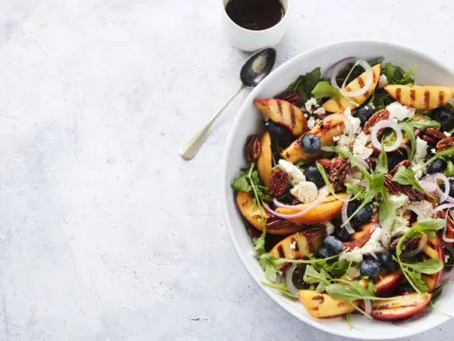 Salat mit Nektarinen, Blaubeeren, Ziegenkäse und Pekannüssen, garniert mit roten Zwiebelringen.