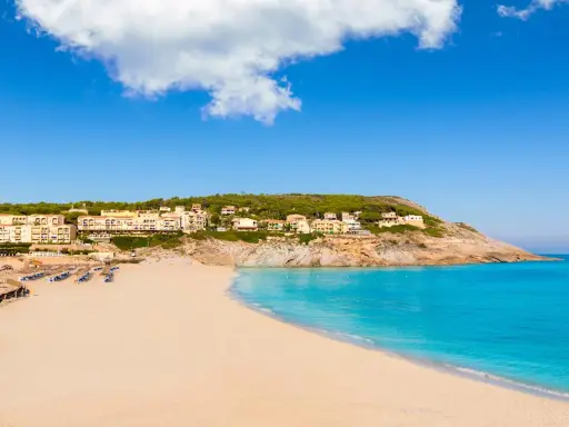 Traumhafter **Spanien Strand** mit feinem Sand, türkisfarbenem Meer und Hotels auf einem Hügel.