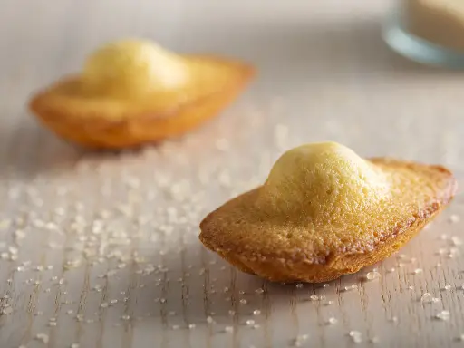 Deux madeleines dorées, parsemées de sucre, prêtes à être dégustées. Une invitation à la recette madeleine parfaite.