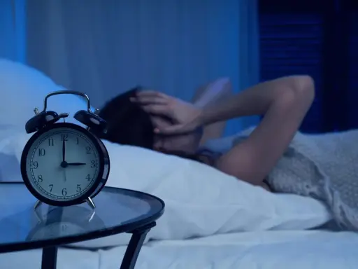 Eine Frau hält sich im Bett die Ohren zu, während ein Wecker auf 3 Uhr steht. Warum wache ich immer um 3 Uhr auf?