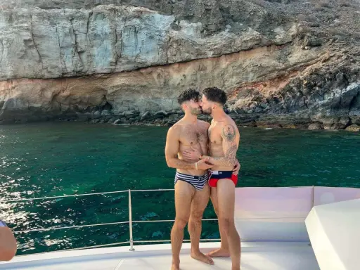 A loving gay couple shares a kiss on a boat, enjoying the stunning scenery of the Canary Islands.
