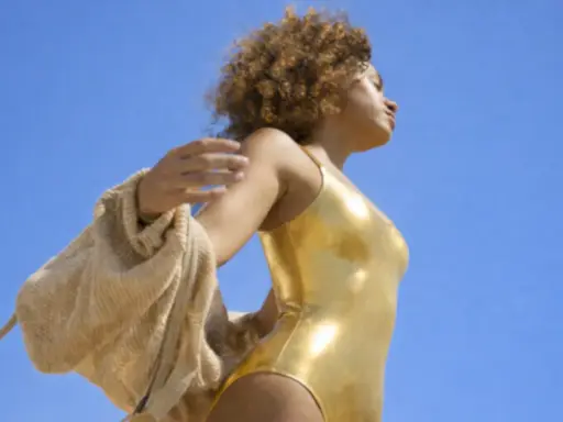 Femme en maillot doré, bras écartés, profitant du soleil. Une belle façon de préparer sa peau au soleil.