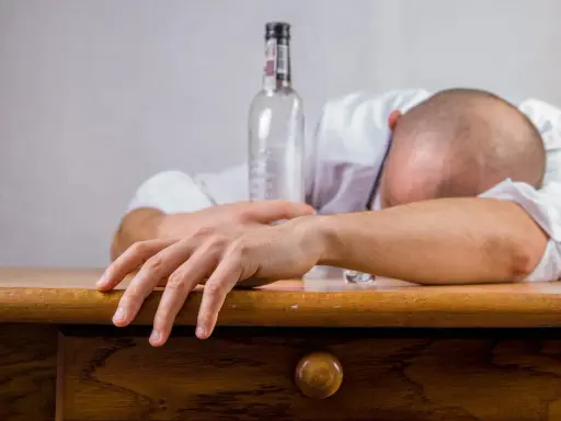 Mężczyzna śpi na stole obok pustej butelki. Zastanawiasz się, co wypić przed alkoholem, by uniknąć takiego losu?