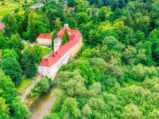 Zamek na skale w Trzebieszowicach, otoczony bujną zielenią, malowniczo wznosi się nad rzeką.