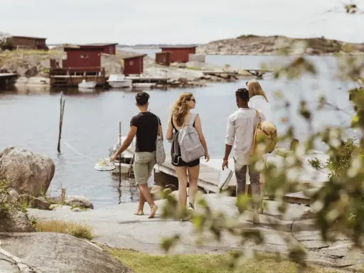 Vänner njuter av en promenad längs vattnet vid röda fiskestugor, en perfekt bild av eco tourism i Sverige.