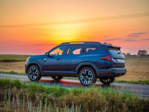 Ciemnoniebieski Dacia Bigster 2025 na tle zachodzącego słońca, na wiejskiej drodze.