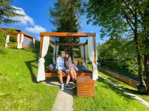 Para zakochanych cieszy się chwilą podczas wyjazdu na weekend. Siedzą na łóżku pod baldachimem, otoczeni zielenią i strumykiem.