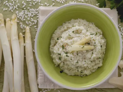 Delicioso risotto de espárragos cremoso, adornado con espárragos blancos y perejil picado. Acompañado de espárragos frescos y trozos de queso parmesano.