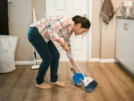 Mujer barriendo el suelo con escoba y recogedor, aplicando trucos de limpieza para mantener el hogar impecable.
