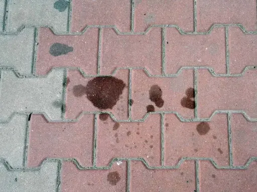 Stare plamy z oleju na kostce brukowej tworzą ciemne ślady, świadczące o dawnych wyciekach.