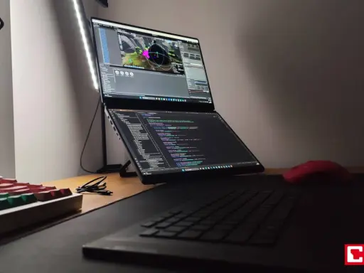 Na biurku laptop z dwoma ekranami, na górnym widać scenę w Unreal Engine 6, na dolnym kod. Obok klawiatura i czerwona myszka.