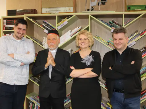 Jacek Ostrowski z książkami w kolejności. Grupa osób pozuje na tle regałów z książkami.