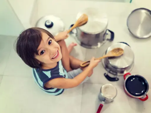 Niño sonriente jugando con ollas y cucharas de madera, creando sus propios instrumentos musicales caseros.