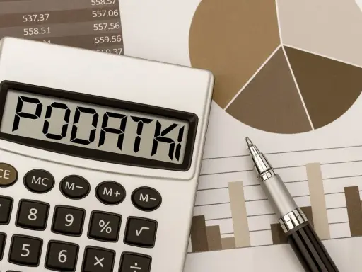 Kalkulator z napisem "PODATKI" obok wykresów i długopisu. Obliczenia podatku od sprzedaży działki.