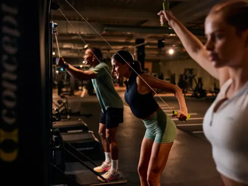 Drei Personen machen ein intensives AMRAP Workout an Kabelzügen. Sie ziehen die Griffe nach hinten und trainieren so ihren Rücken.