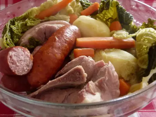 Un plat typique auvergnat : saucisses, porc, pommes de terre, carottes et chou savoyard mijotés dans un grand bol en verre.