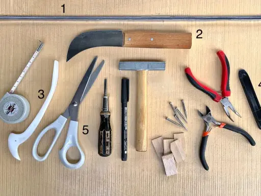 Outils pour le **matériel vitrail** : ruban à mesurer, ciseaux, couteau, marteau, pinces, clous et petits morceaux de bois.