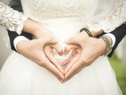 Manos formando un corazón, celebrando 2 años de casados. Vestido de novia blanco y traje negro.