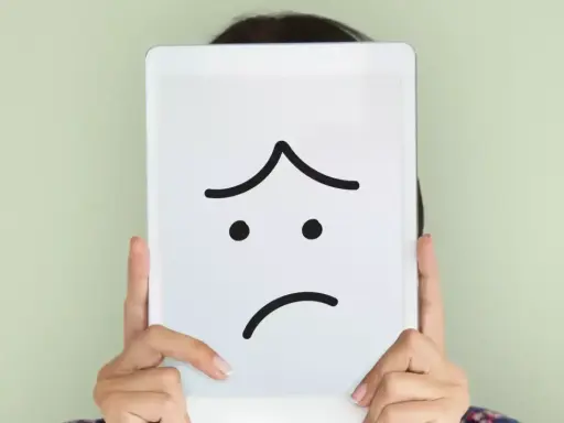 Una persona nasconde il volto dietro un tablet con un'espressione triste disegnata. La famiglia invischiata Minuchin potrebbe sentirsi così.
