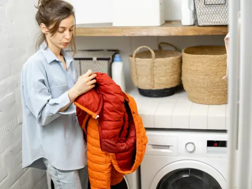 Mujer revisa un anorak naranja y rojo, preparándose para saber como lavar un anorak en la lavadora.
