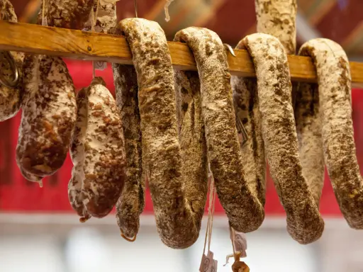 Saucissons secs, une spécialité culinaire auvergnate, pendent sur un support en bois.