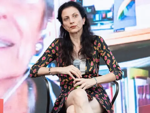 Veronica Tomassini, la cui età non è specificata, con un microfono in mano, indossa una giacca con fantasia floreale.
