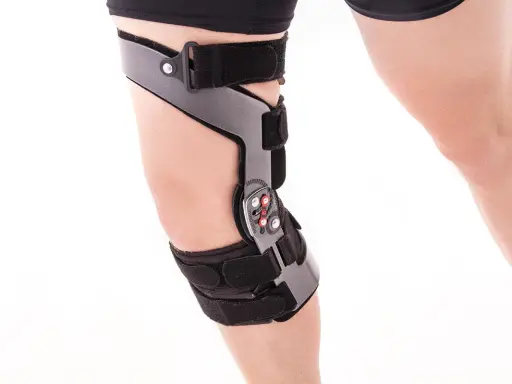 Stabilizator na kolano z metalowymi elementami i paskami na białym tle.