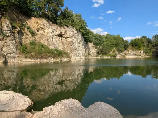 Spokojny zalew kamieniołom w Zabierzowie, z odbijającymi się w wodzie skalnymi ścianami i zielenią drzew.