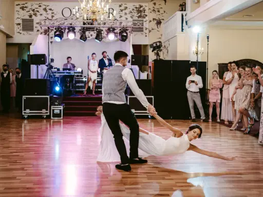 Para młoda wykonuje widowiskowe podnoszenia w tańcu, goście z zachwytem obserwują ich występ.