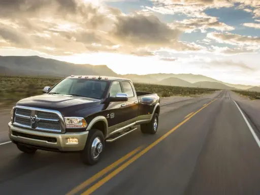 Ciemnobrązowy Dodge Ram 2500 z dwoma rzędami kół jedzie pustynną drogą o zachodzie słońca.
