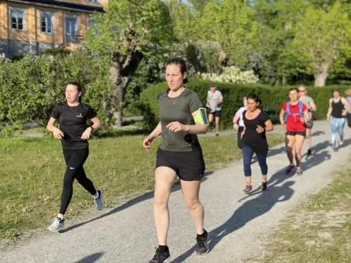 En grupp löpare på en grusväg, kanske på väg att klara 1 mil. Solen skiner och träden är gröna.