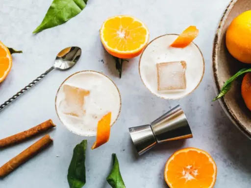 Zwei cremige Gin Sours mit Eis und Orangenzesten, garniert mit Zimtstangen und frischen Mandarinen.